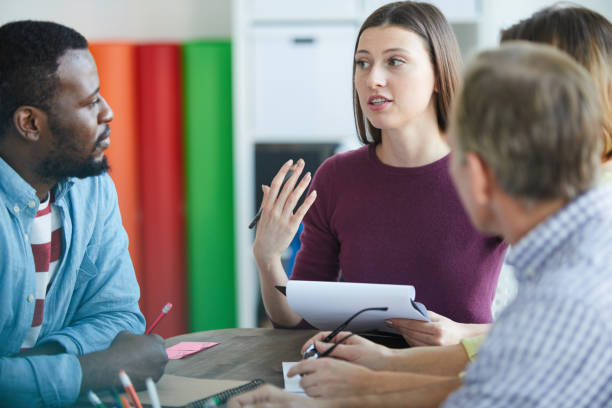 istock Content confident young woman sitting at table and holding clipboard while expressing her opinion at meeting 1132400434