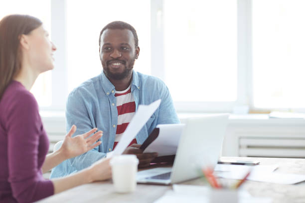 istock Content positive multi-ethnic creative specialists sitting at table and discussing sketches while elaborating advertising campaign 1132400487