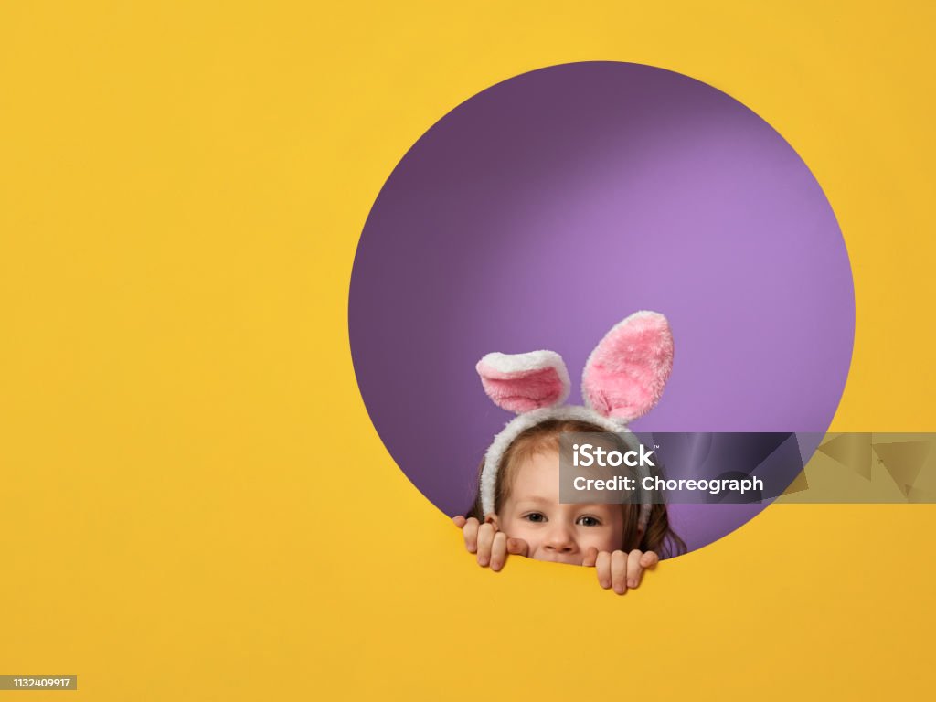child on Easter day Cute little child wearing bunny ears on Easter day. Girl on yellow and violet background. Easter Stock Photo
