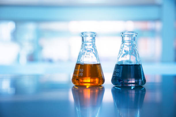 two glass flasks with orange and black solution in chemical science laboratory background two glass flasks with orange and black solution in chemical science laboratory background beaker photos stock pictures, royalty-free photos & images