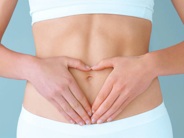 Become healthy and your body will love you for it Studio shot of a healthy woman using her hands as a heart shape frame on her stomach against a purple background navel stock pictures, royalty-free photos & images