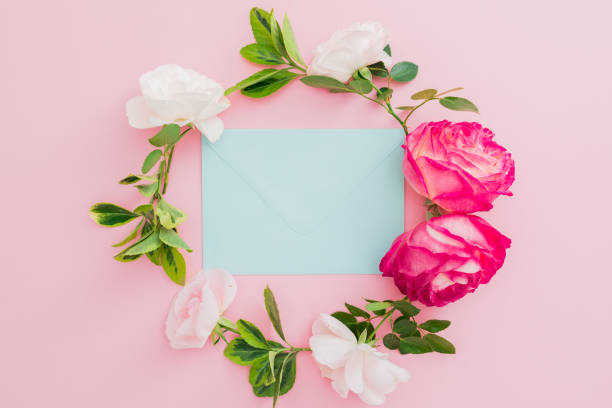 istock Floral frame with roses flowers and blue envelope on pink background. Flat lay, top view. 1132424398