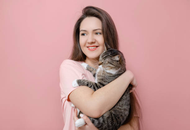 istock young attractive woman hugging cat in hands, pink background 1132425955