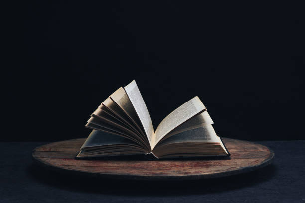 istock One open old book on a round wooden table. Beautiful dark background. 1132426053