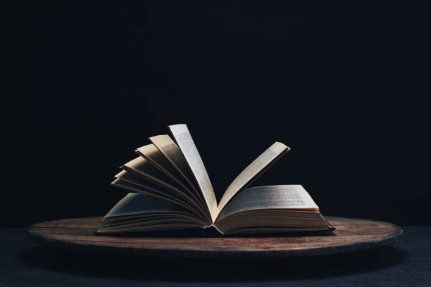 istock One open old book on a round wooden table. Beautiful dark background. 1132426081