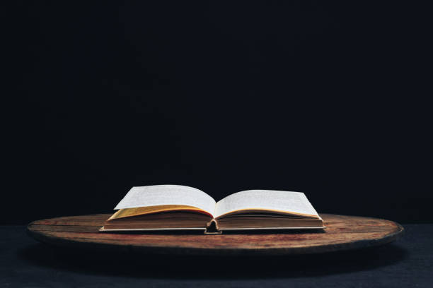 One open old book on a round wooden table. Beautiful dark background.