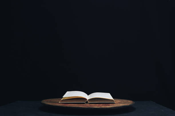 istock One open old book on a round wooden table. Beautiful dark background. 1132426094