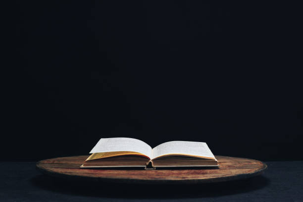 istock One open old book on a round wooden table. Beautiful dark background. 1132426104