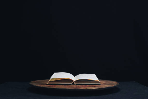 istock One open old book on a round wooden table. Beautiful dark background. 1132426615