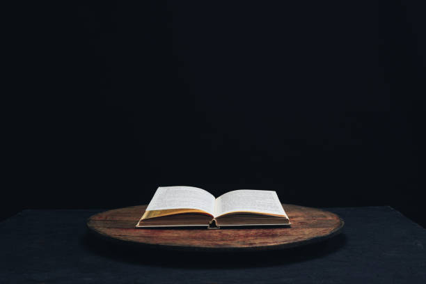 istock One open old book on a round wooden table. Beautiful dark background. 1132426623