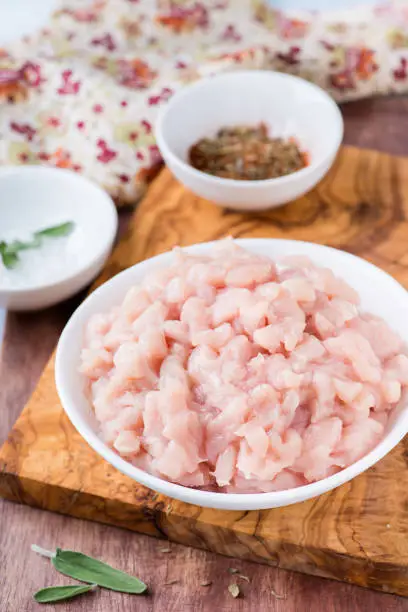 Fresh raw chopped chicken meat in a bowl with seasoning and sage, selective focus