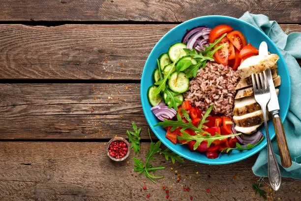 Grilled chicken breast. Fried chicken fillet and fresh vegetable salad of tomatoes, cucumbers, pepper, lettuce and arugula leaves. Chicken meat with salad. Healthy food. Flat lay. Top view. Wooden background