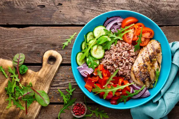 Grilled chicken breast. Fried chicken fillet and fresh vegetable salad of tomatoes, cucumbers, pepper, lettuce and arugula leaves. Chicken meat with salad. Healthy food. Flat lay. Top view. Wooden background