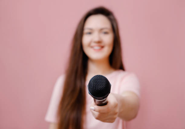 istock young woman with microphone in hand on pink background extends hand to camera 1132429519