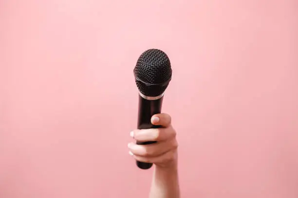 Photo of microphone in female hand on pink background