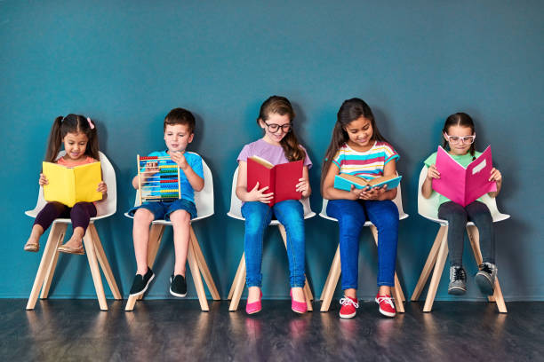 Stay curious Studio shot of a group of kids sitting on chairs and reading books against a blue background people in a row photos stock pictures, royalty-free photos & images