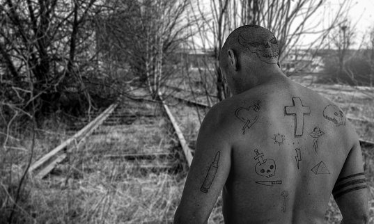 Guy with doodle tattoos walking on abandoned railroad track. Criminal, convict escape and prison tattoo concept. Image montage.