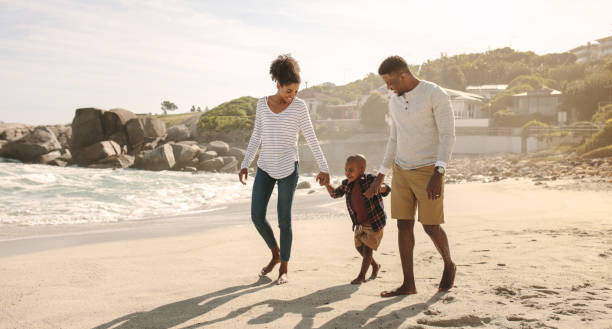 African family on beach walk Family of three taking a walk along the sea shore. Man and woman holding hands of son and walking on beach. holding hands photos stock pictures, royalty-free photos & images