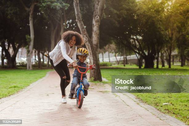Mamá Enseñando A Su Hijo Andar En Bicicleta En El Parque Foto de stock y más banco de imágenes de Niño