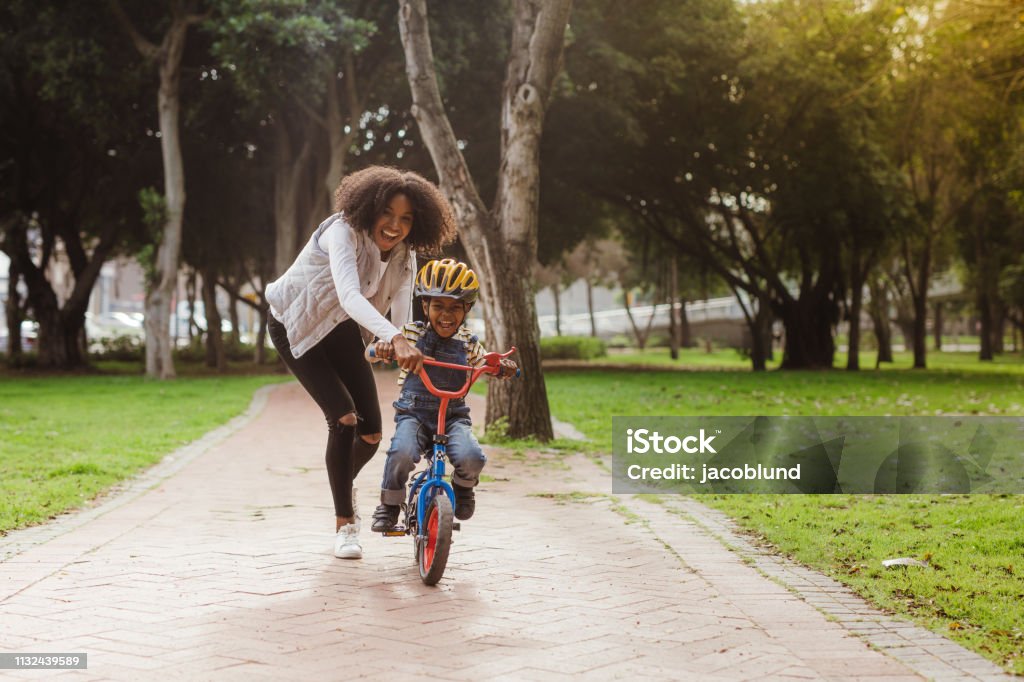 Mom teaching her son biking at park Cute boy learning to ride a bicycle with his mother. Woman teaching son to ride bicycle at park. Child Stock Photo
