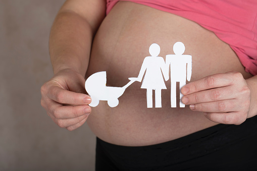 Young pregnant between 30 and 35 years old woman keeps paper cutouts of a family. Closeup