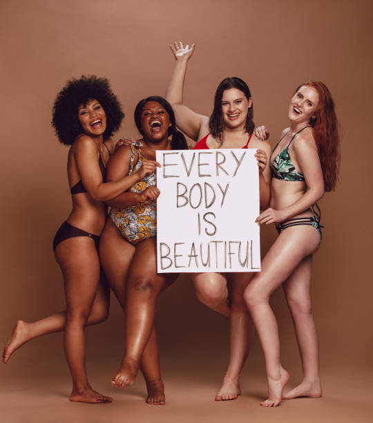 Cheerful female group with every body is beautiful signboard Cheerful group of women holding a every body is beautiful signboard over brown background. Multiracial females of different figure and size looking excited together. beauty in nature vertical africa southern africa stock pictures, royalty-free photos & images