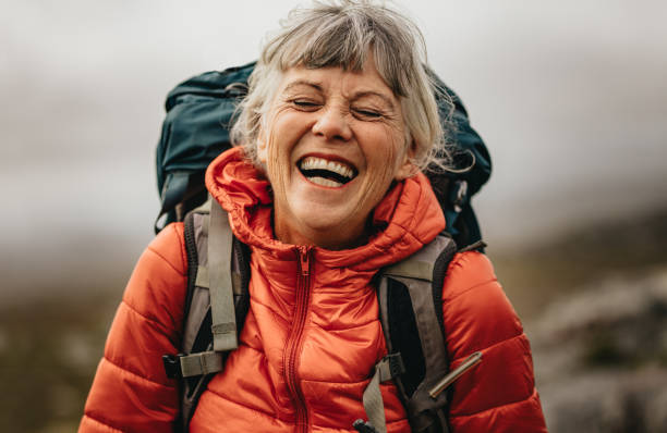 Senior woman enjoying her hiking trip Close up of a senior woman wearing jacket and backpack laughing with eyes closed. Portrait of a woman hiker laughing during her trekking. senior women stock pictures, royalty-free photos & images