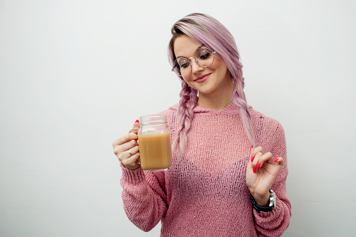 Trendy young woman drinking coffee milkshake. Girl with jar-mug on