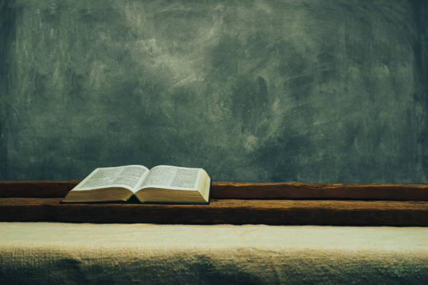 istock Open Bible on a old table. Beautiful gray wall background. Religion concept. 1132446780
