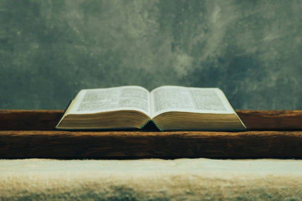 istock Open Bible on a old table. Beautiful gray wall background. Religion concept. 1132447192
