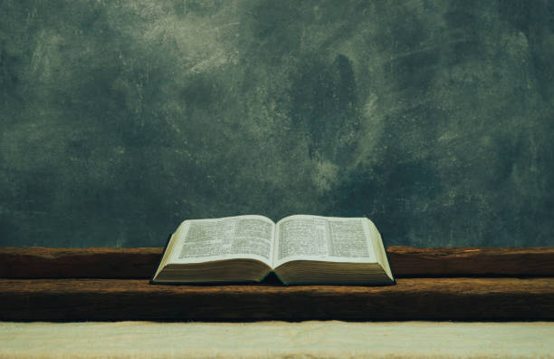 istock Open Bible on a old table. Beautiful gray wall background. Religion concept. 1132447841