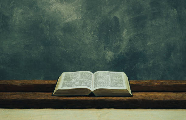 istock Open Bible on a old table. Beautiful gray wall background. Religion concept. 1132447860