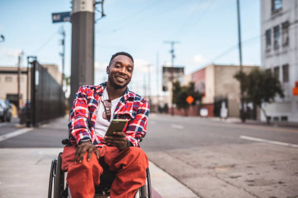 retrato de un hombre afroamericano discapacitados en una silla de ruedas con teléfono inteligente al aire libre - physical impairment smiling front view looking at camera fotografías e imágenes de stock