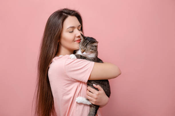 istock young attractive woman hugging cat in hands, pink background 1132449296