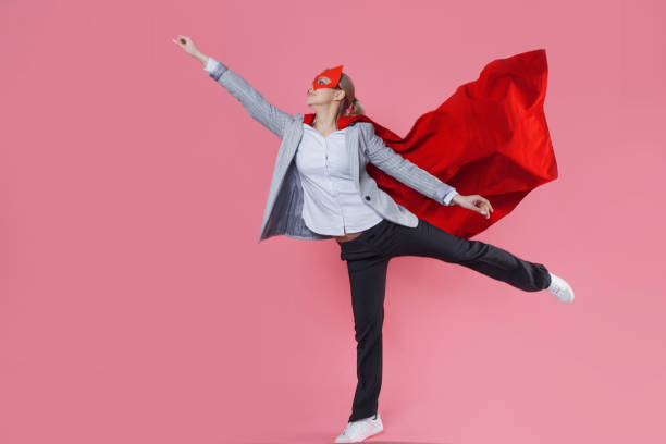 Young attractive woman superhero. Girl in a business suit and a mask with red cloak of hero. stock photo