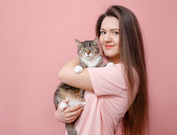 istock young attractive woman hugging cat in hands, pink background 1132457083