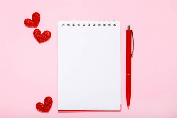 istock White paper, red pen and hearts on a pink background. 1132459617