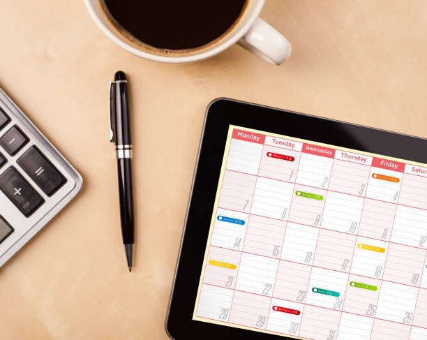 Tablet pc showing calendar on screen with a cup of coffee on a desk Workplace with tablet pc showing calendar and a cup of coffee on a wooden work table close-up ipad calculator stock pictures, royalty-free photos & images