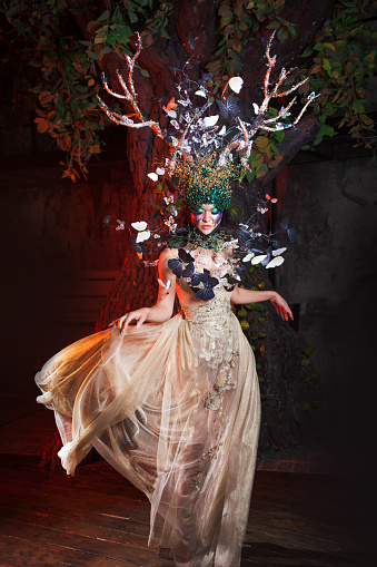 natural nymph with horns like branches of a tree and butterflies circling around. Fantasy style costume, young beautiful girl in the image of flora