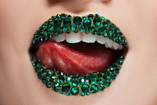 Green lips covered with rhinestones. Beautiful woman with Green lipstick on her lips, tongue licked her teeth