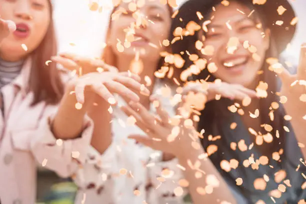 Blurred asian friends having fun throwing confetti at party outdoor - Young trendy people enjoying fest event - Hangout, friendship, trends and youth concept - Defocused photo