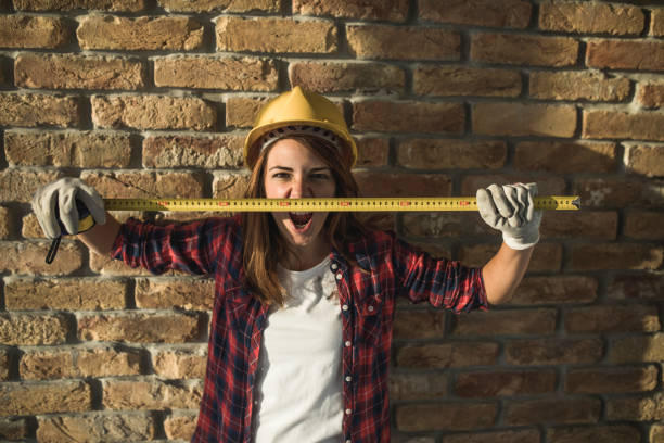 istock Female manual worker shouting while holding tape measure against the wall. 1132476022