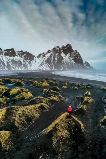 Exploring Stokksnes bay Mature woman standing in a sand dune looking at Stokksnes bay with Vestrahorn mountain in the background. spectacular view stock pictures, royalty-free photos & images
