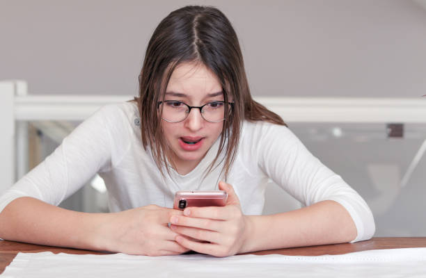 Cute tween girl looking at smartphone in her hands with scared shocked and surprised face expression. Child and gadget concept. Internet and social networks safety. Bulling stock photo