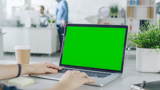 Close-up of a Man's Hands Working on Green Screen on a Laptop. In Background Blurred and Brightly Lit Office where One Man Approaches the Other and They Have Discussion.