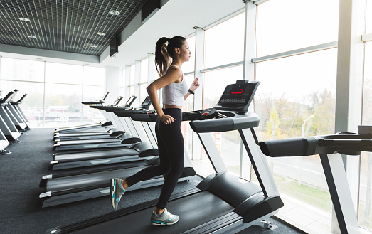 Sports woman training on treadmill near the window in gym
