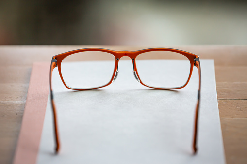 Orange eye glasses with white notebook on wooden table, Bokeh  background, Close up & Macro shot, Selective focus, Stationery concept
