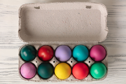 Top view of colorful easter eggs in box on white wooden table