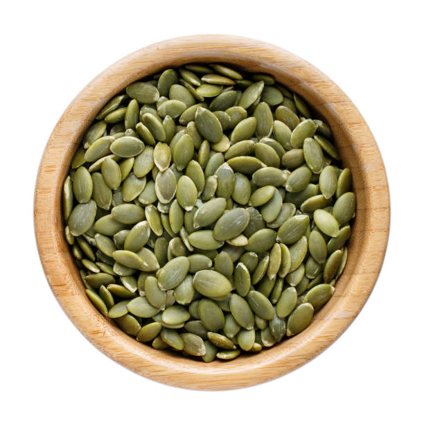 Dried pumpkin seeds in wooden bowl isolated on white. Top view.