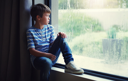Shot of a sad young boy watching the rain through a window at home